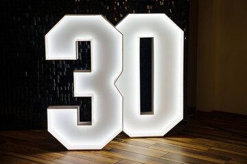 The lamp in the shape of the number 30 strip against the background of a wall of sequins.