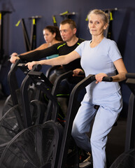 Focused mature woman using elliptical machine in gym