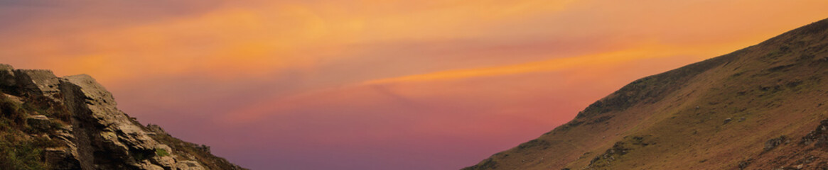 Orange sky at sunset and mountains along the edges of the image with free space for text, copy space. Wide panoramic view of beautiful clouds between mountains