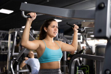 Fototapeta na wymiar Fit young woman working out at shoulder press machine in gym