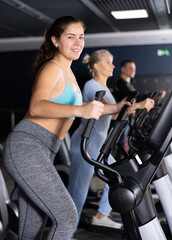Fototapeta na wymiar Sporty young woman using elliptical machine in gym