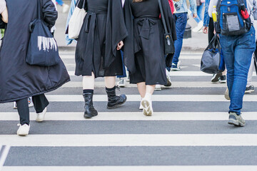 Fototapeta na wymiar Pedestrians crossing crosswalk. Young people in black clothes, Stylish hipster girls walking city on weekend day