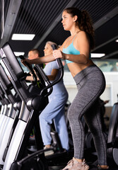 Portrait of concentrated young girl working out on elliptical machine in gym. Active lifestyle concept