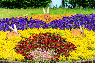 Colorful flowerbed of pansies and daisies decorated with wooden Easter bunnies in park at spring