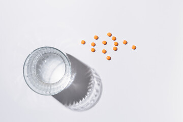 Transparent glass of water with hard shadow from light next to orange pills on white isolated background. Health, useful supplements, vitamins. pharmaceutical and medicine for disease concept.