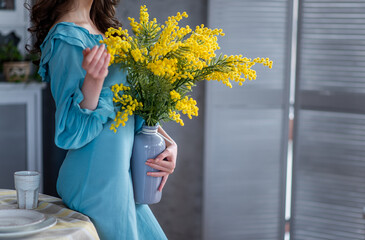 Faceless girl in a blue dress holds a vase with a bouquet of yellow mimosa in her hands. Spring,...