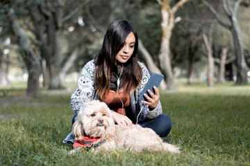 Girl watching her phone next to her dog in the park. Girl sitting in the park with her dog. 