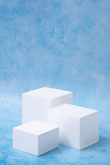 White cubes beauty cosmetic new product podium on blue background. Promotion sale, presentation. Geometric shapes. Vertical object placement.