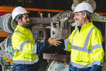 Two senior male engineers and workers wearing safety vests and jacket along with hardhat or helmet while clenching hands and making a fist standing in front of machine in warehouse