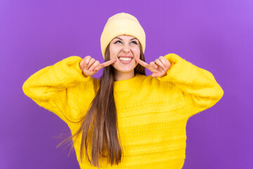 Close up portrait of a young, cheerful woman isolated on purple studio background in yellow woolen pullover smiling