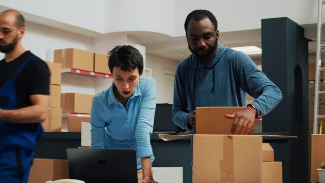 Cheerful owners doing highfive symbol in storage room, feeling happy about finishing packing order with merchandise. Young team of people preparing products in cardboard boxes.