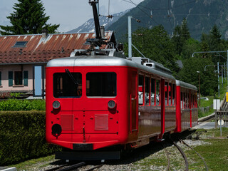 Fototapeta premium Iconic red mountain train in Chamonix, set against a stunning alpine backdrop. A historic and scenic journey through breathtaking landscapes of the French Alps