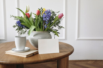 Easter breakfast still life with cup of coffe, book. Colorful spring floral bouquet with tulips and hyacinth flowers. Blank greeting card, invitation. Birthday, Mothers day concept. Elegant interior.