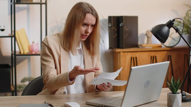 Stressed young businesswoman working looking at unpaid bank debt bills, doing paperwork, planning budget, calculate finances mortgage payments at office. Displeased freelancer woman throws paper bills