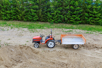 A mini-tractor with a trailer on a construction site transports and pours earth.