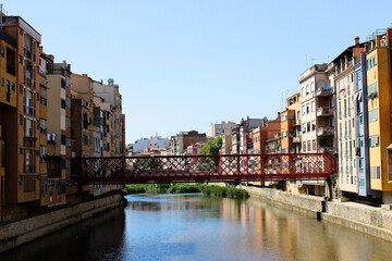 colorful 4- or 5-story buildings border a watercourse, which partially reflects the color of the buildings, with the two banks connected by a red metal bridge