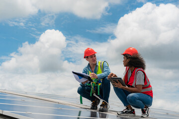 Two young engineer and inspector wearing safety vest and hard helmet inspecting solar panel by...