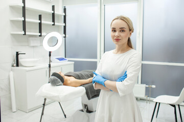 portrait of cosmetologist girl in cosmetology clinic, young dermatologist doctor in uniform stands with folded arms