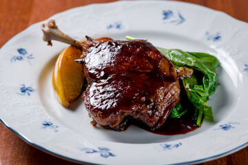 Duck leg confit on plate on wooden table macro close up