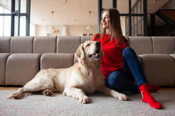 young girl plays with dog breed golden retriever at home on floor, woman with pet together lies on mat near the sofa