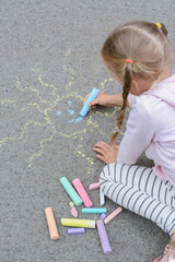 Naklejka premium Little child drawing sun with chalk on asphalt