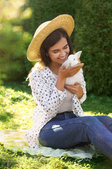 Happy woman with cute rabbit on green grass outdoors