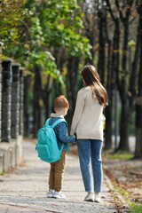 Young mom taking her son to school, back view