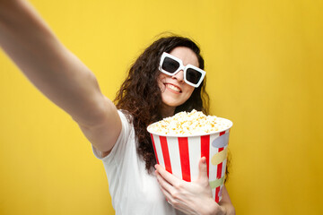 Obraz premium cheerful curly girl viewer in 3d glasses holds popcorn and takes selfie on yellow background