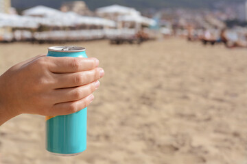 Woman holding aluminum can with beverage on beach, closeup. Space for text