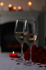 Glasses of white wine, burning candle and rose flowers on grey table against blurred lights. Romantic atmosphere