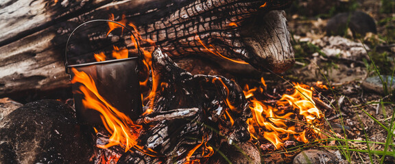 Kettle hanging over fire. Cooking food at fire in wild. Beautiful big log burns in bonfire...