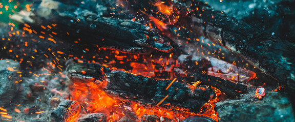 Vivid smoldered firewoods burned in fire close-up. Atmospheric background with orange flame of campfire. Full frame image of bonfire. Warm whirlwind of glowing embers and ashes in air. Sparks in bokeh