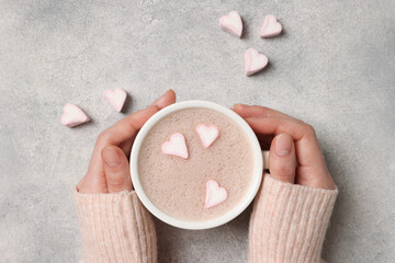 Woman holding cup of aromatic coffee with heart shaped marshmallows at light grey background, top view