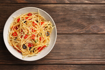 Bowl of delicious pasta with olives, tomatoes and parmesan cheese on wooden table, top view. Space for text