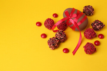 Tasty chocolate egg with red ribbon and candies on yellow background, flat lay. Space for text
