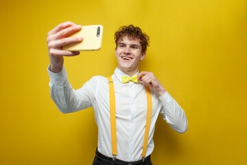 guy in bow tie and suspenders takes selfie on yellow isolated background, nerd photographs himself...