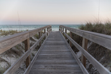 Straight wooden pathway with railings in between sand dunes against the ocean and horizon sky. Wooden walkway near the protected sand dune with grasses with views of ocean waves in Destin, Florida.