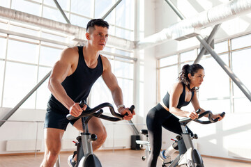 athletic couple of cyclists train on static bicycle simulator, man trainer and fitness woman go in...