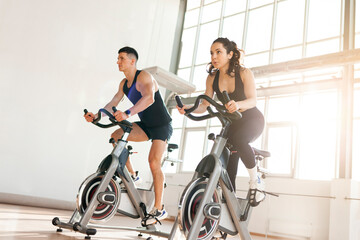 athletic couple of cyclists train on static bicycle simulator, man trainer and fitness woman go in for sports together