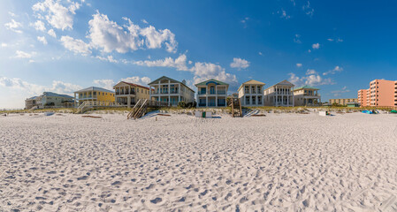 Fototapeta na wymiar Beautiful and lavish beach homes overlooking white sandy shore in Destin Florida. Facade of waterfront multi-storey houses against blue sky and clouds background.