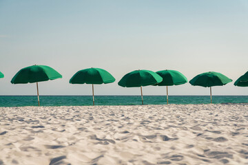 Outdoor green beach umbrellas on a white sand beach at Destin, Florida. There is a row of umbrellas...