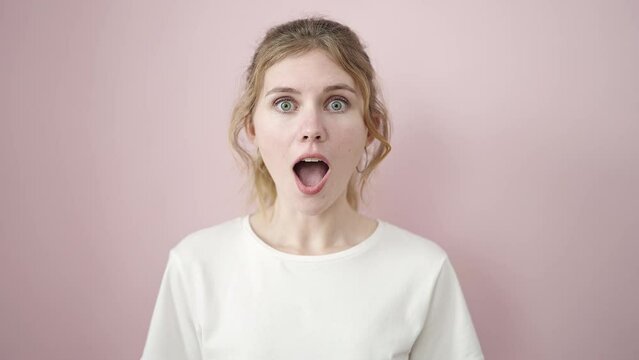Young blonde woman standing with surprise expression over isolated pink background