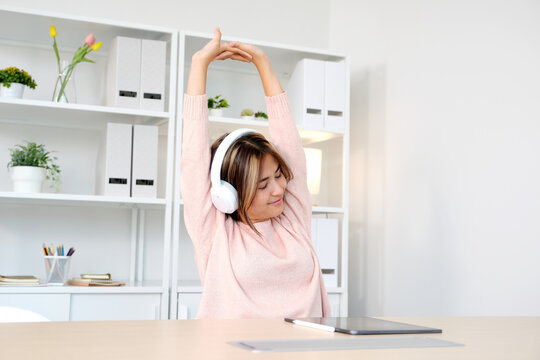 Young asian woman with headphones stretching for relax after working