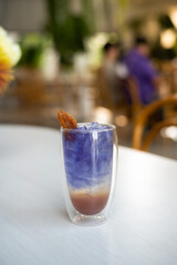 A clear plastic glass contains a blend of butterfly pea juice and bael.