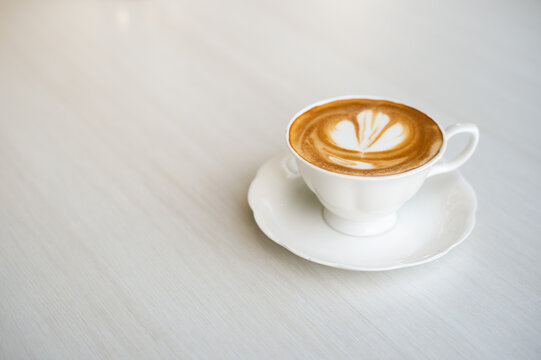 A hot coffee latte adorned with a leaf image is placed on a black table at a coffee shop.