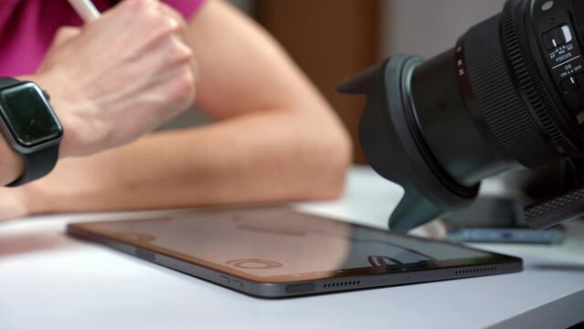 Hand draws a line on a graphic tablet for drawing with pencil, the camera lens shoots. Close-up of a designer drawing on a tablet. Illustrator's work being filmed for a course on online careers