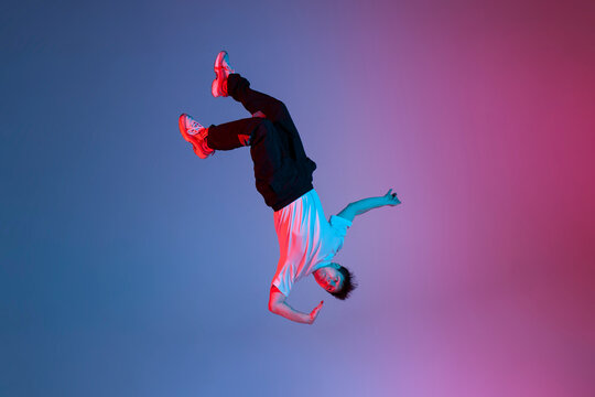 young guy falls upside down in the air, man levitates and flies down in neon lighting, acrobat dancer flies in a jump