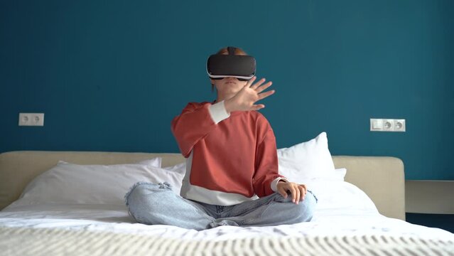 Teenager using virtual reality glasses at home select 3D metaverse menu for education online. Girl touch air for VR experience choice app items working in gadget interface. Digital simulator for game 