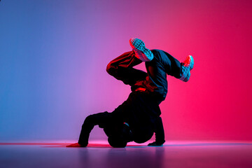 dancer doing acrobatic trick and dancing breakdance in neon red and blue lighting, young energetic guy - obrazy, fototapety, plakaty