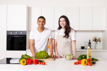 multiracial couple in kitchen preparing salad together, american guy and european girl preparing veggie food